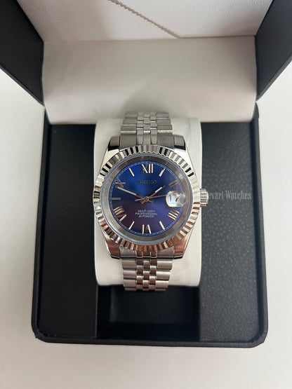 Datejust (Royal Blue Roman) Seiko NH35 automatic mod watch. A blue dial watch with a silver fluted bezel and jubilee bracelet shown in a box from a front view.