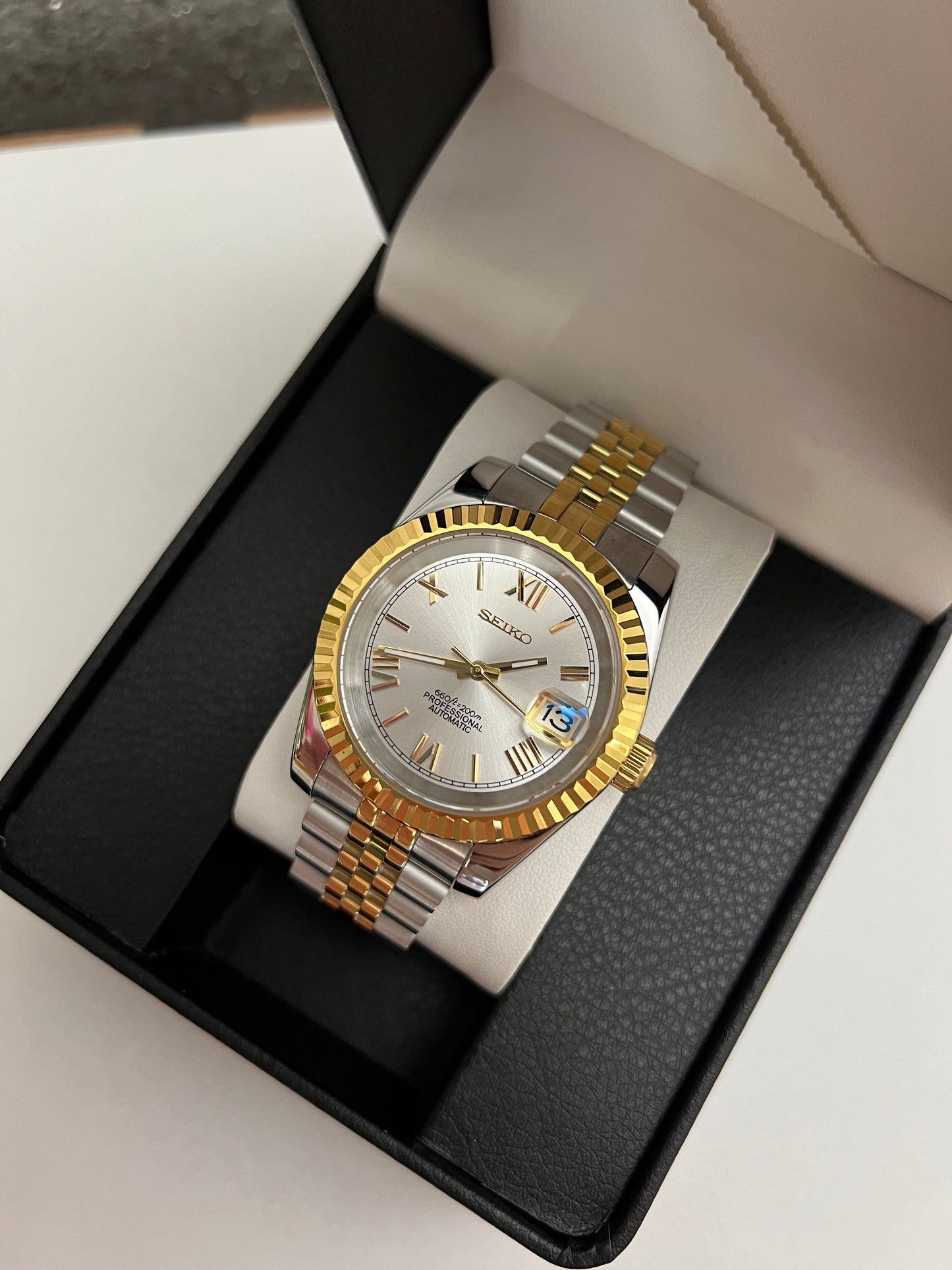 Datejust (Two-Tone White Roman) Seiko NH35 automatic mod watch. A silver dial watch with a gold fluted bezel and two tone jubilee bracelet is angled inside a black box.