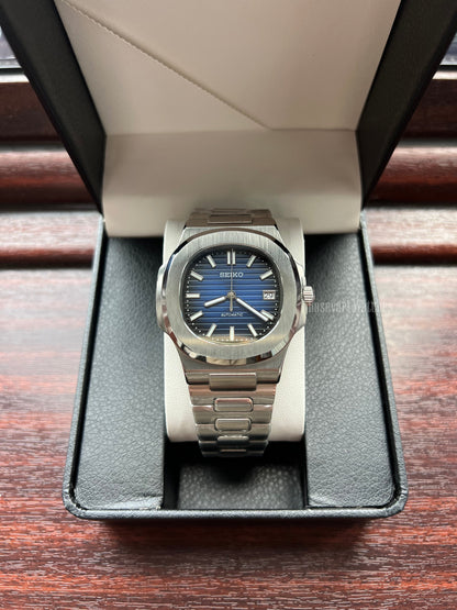 Nautilus (Royal Blue) Seiko NH35 automatic mod watch. A blue dial watch with a silver bezel and metal link bracelet shown in a straight on shot inside a box.
