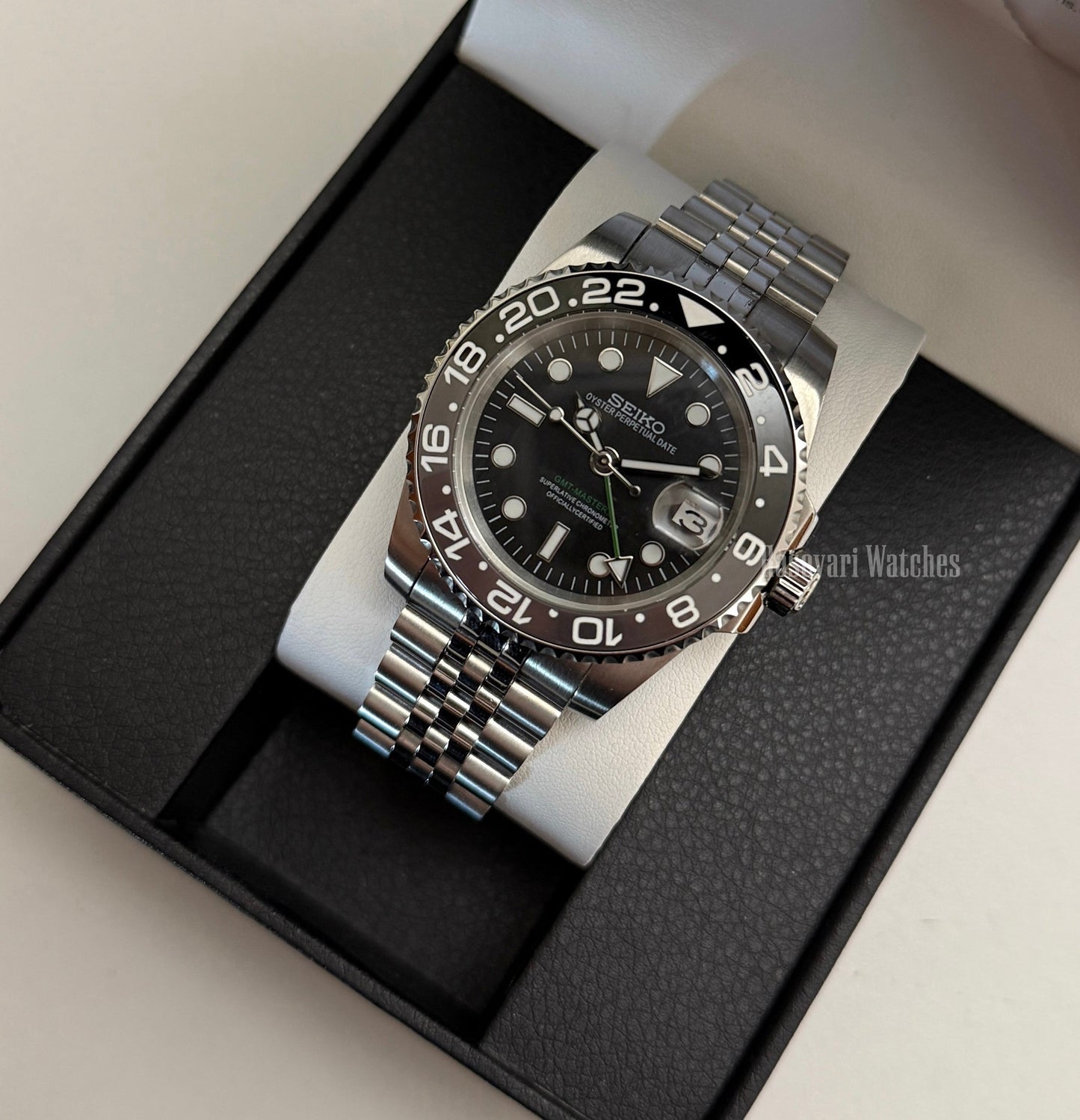 GMT (Bruce Wayne) Seiko NH34 GMT automatic mod watch. A full watch shot of a black dial watch with a black bezel inside a black presentation box.