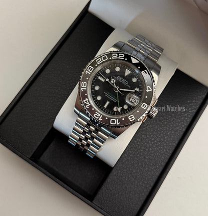 GMT (Bruce Wayne) Seiko NH34 GMT automatic mod watch. A full watch shot of a black dial watch with a black bezel inside a black presentation box.