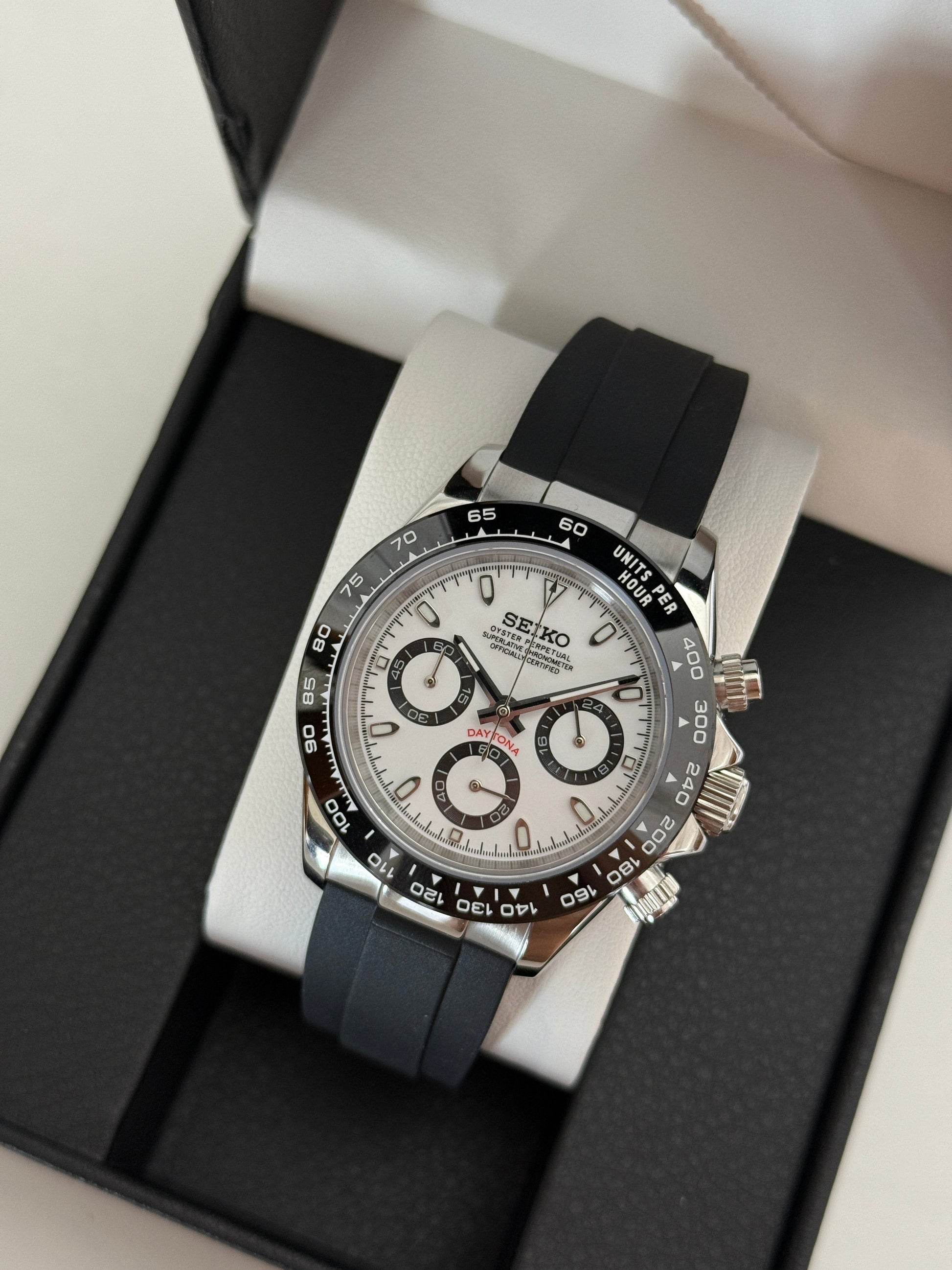 Daytona (Panda) Seiko VK63 meca-quartz chronograph mod watch. A high angle full watch shot in a box showing a white dial with black sub dials and a black bezel.