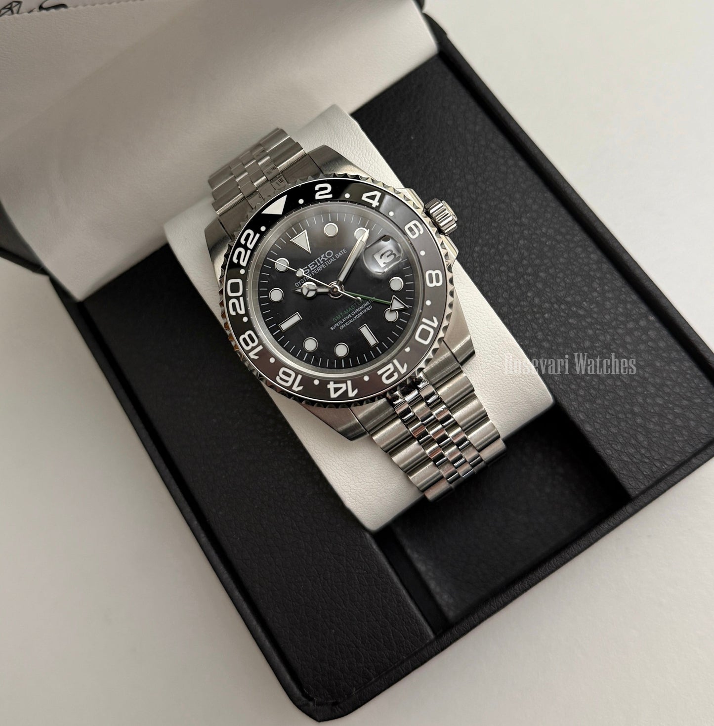 GMT (Bruce Wayne) Seiko NH34 GMT automatic mod watch. A full watch shot of a black dial watch with a black bezel inside a black presentation box.